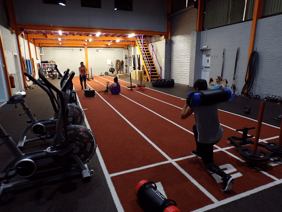 gym members lifting weight and pulling sleds on four lane track