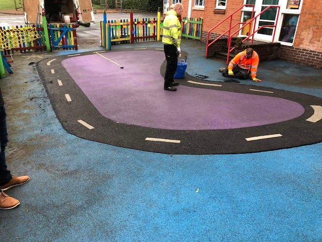 installers inspecting a dirty wet pour rubber playground roadway