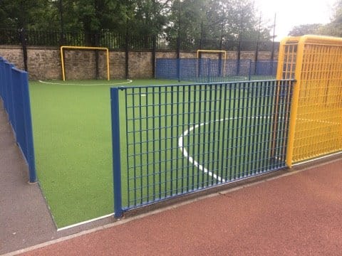 small primary school green sports surface with railings and a goal