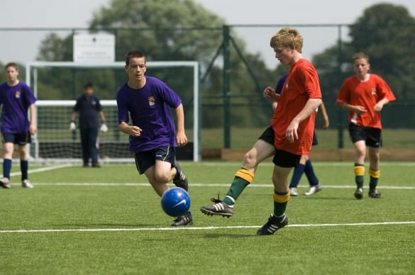 secondary school pupils playing football on artificial grass pitch
