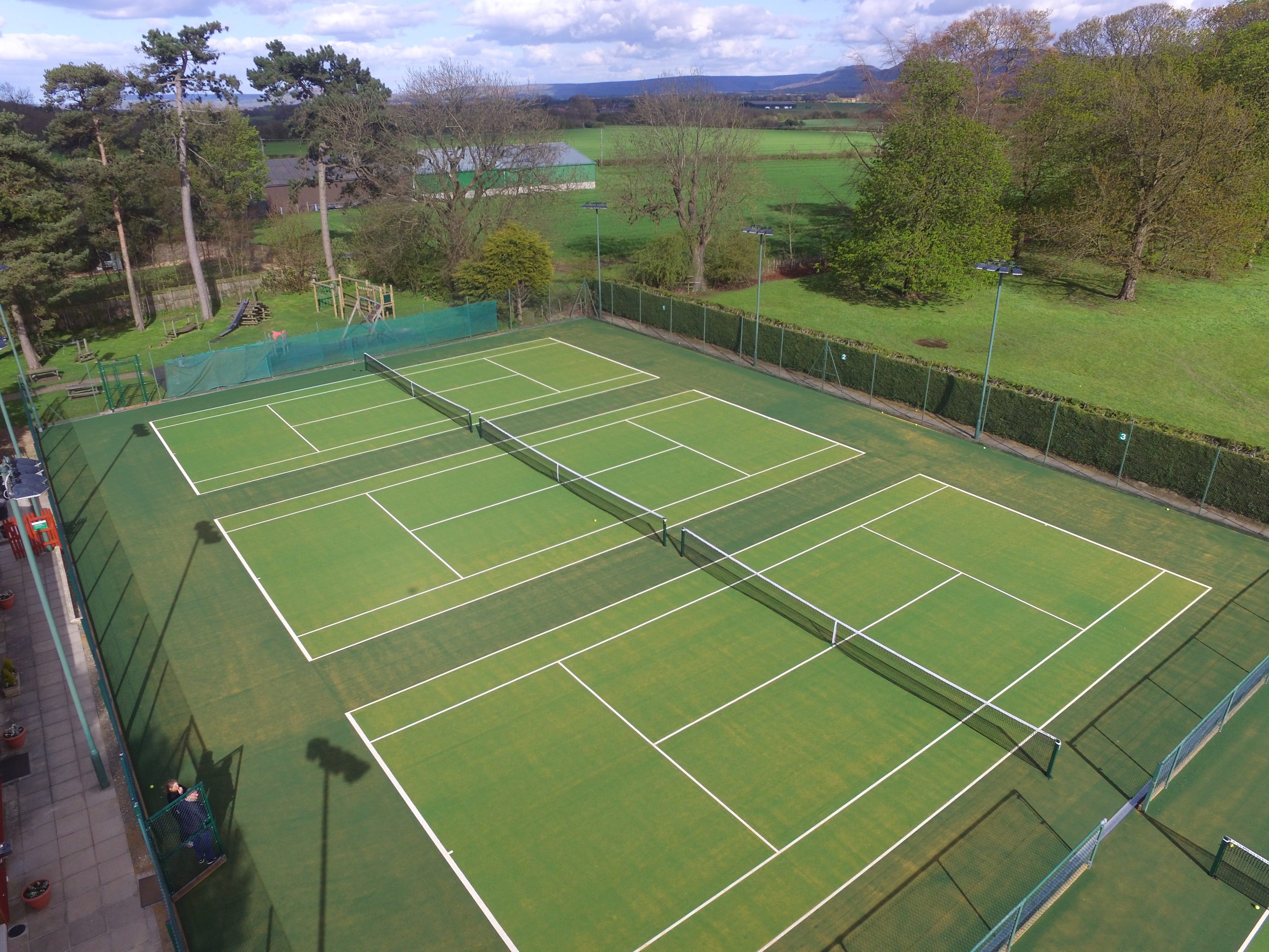 drone footage of three astroturf green tennis courts